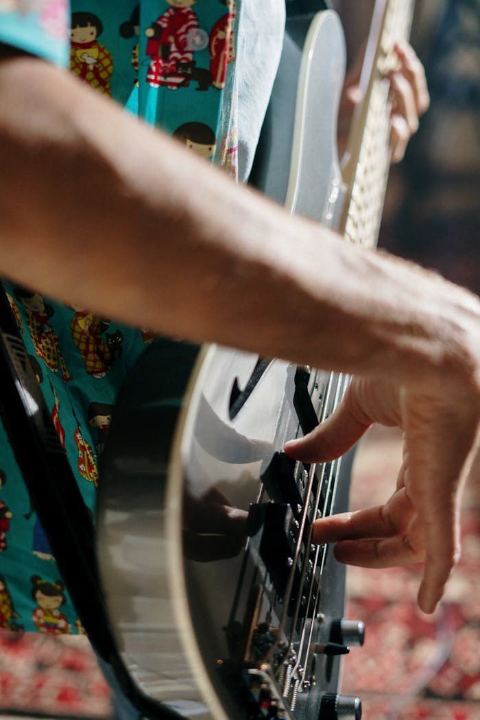 A musician wearing a patterned shirt plays an electric guitar, highlighting the intricate details of the instrument.